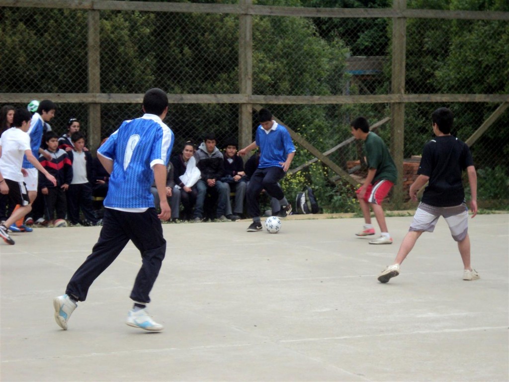 Miembros de la alianza naranjo-amarilla (usando el peto azul) manejan el balón durante el partido de fútbol masculino contra la alianza negro-calipso.