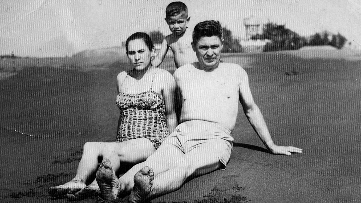 María Eliana Poblete Carvajal y Emelino Pino Yañez, junto a su hijo Miguel Pino Poblete, toman el sol en la playa las Terrazas, frente a la avenida Daniel Ortúzar. Al fondo se aprecia la antigua copa de agua y el bosque. Década de 1950.