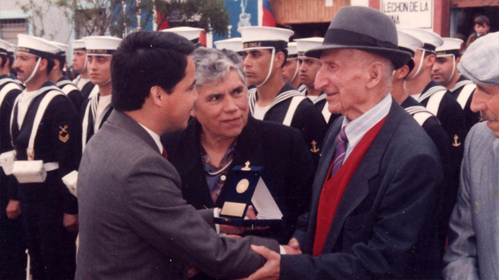El alcalde René Maturana entrega un reconocimiento al exalcalde Basilio Sánchez, en la conmemoración del 100° aniversario de la comuna de Pichilemu. Foto: Biblioteca Pública.